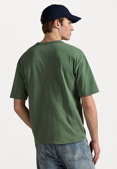 Green, short-sleeve T-shirt made from textured fabric, featuring a crew neckline and a relaxed fit, paired with faded blue jeans.