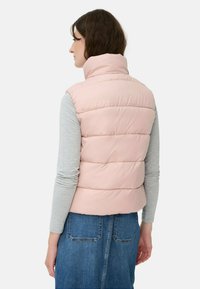 Rosa Pufferweste mit hohem Kragen, horizontalen Nähten und leichtem Design. Getragen über einem grauen Langarmshirt, kombiniert mit einem Jeansrock.