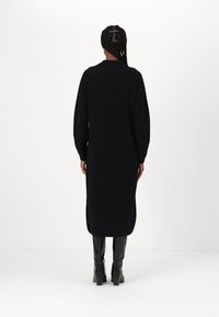 Vestito nero a maniche lunghe con una vestibilità comoda, realizzato in un tessuto morbido, con scollo rotondo e lunghezza fino a metà polpaccio, abbinato a stivali al ginocchio.