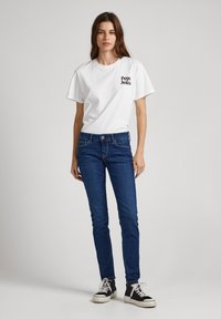 Camiseta de algodón blanca con el logo "Pepe Jeans" en el pecho, combinada con jeans ajustados azul oscuro y zapatillas altas negras.
