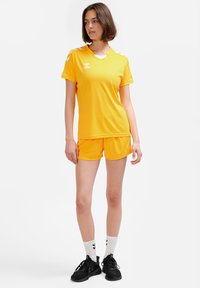 Ljusgul sportuniform med kortärmad tröja och shorts. Tröjan har vita detaljer på axlarna och en V-ringad design.