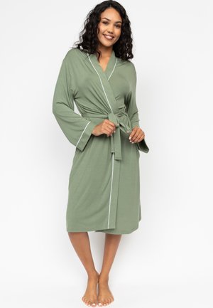 Robe vert olive en tissu doux, avec une fermeture à nouer, des manches évasées et un passepoil blanc le long des bordures. Modèle mi-long.