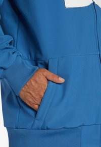 Sweatshirt bleu avec des poignets et un ourlet côtelés. Dispose d'une poche avant avec une texture lisse et des coutures minimales, mettant en valeur un design épuré.