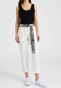 Czarna, bezrękawnikowa bluzka w zestawieniu z białymi spodniami z podwiniętymi nogawkami, które mają pasek w zebrze. Całość uzupełniają białe sneakersy.