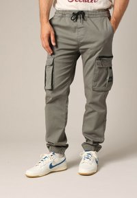 Grijze cargobroek met elastische boorden, een trekkoord taille, meerdere zakken, gemaakt van lichtgewicht stof; gecombineerd met witte sneakers met blauwe accenten.