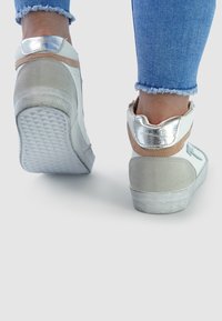 White high-top sneakers with silver accents and tan suede detail, textured sole, smooth leather upper, and frayed hem denim.