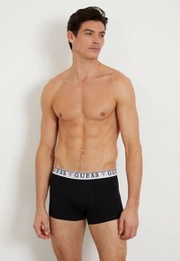 Boxer neri con fascia in vita bianca con il logo "GUESS". Il tessuto appare liscio con un design aderente.