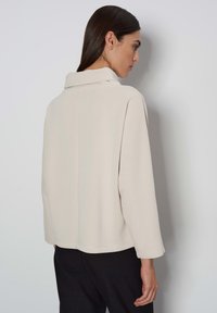 Lichtbeige jas met een gestructureerde kraag, boxy vorm en driekwartmouwen, gemaakt van een gladde stof met subtiele stiksels.