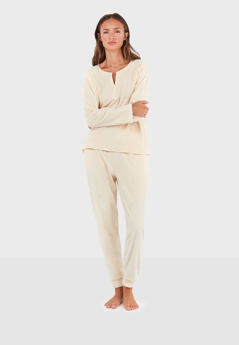 Crème-kleurige pyjama set van zachte stof. Het topje heeft een ronde halslijn en lange mouwen, terwijl de broek elastische boorden en subtiele patronen heeft.