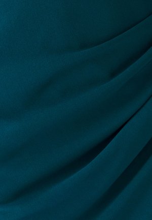 Tirkīzzila audums ar gludu tekstūru, kas atspoguļo izliektas krokas, radot mīkstas ēnas un izgaismojumu, norādot uz vieglu, plūstošu dizainu.