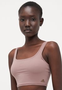 Light pink sports bra with a square neckline and thin straps. Features subtle branding in gold at the bottom left. Smooth texture.