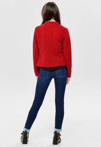 Rote strukturierte Jacke mit passendem Design, kombiniert mit dunkelblauen Skinny-Jeans mit umgeschlagenen Säumen und Ankle-Boots.