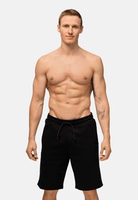Pantaloni corti atletici neri con cintura elastica e cordino. Il tessuto sembra morbido con una superficie liscia. Modello in piedi.