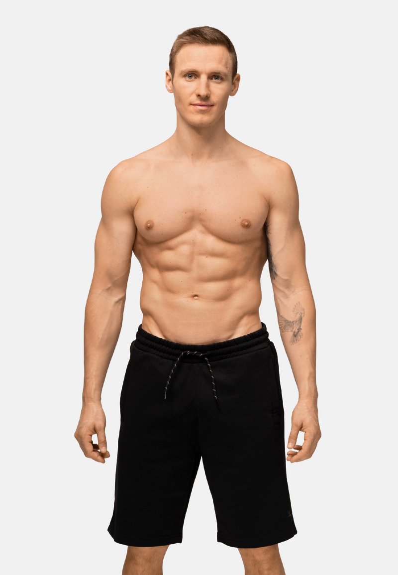 Pantaloni corti atletici neri con cintura elastica e cordino. Il tessuto sembra morbido con una superficie liscia. Modello in piedi.