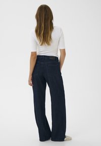 Mörkblå vida jeans i denim, med midjehöjd och standard femfickorsdesign. Bakifrån syns en etikett vid midjan.