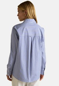 Modrá a biela pruhovaná košeľa s plisovaním na chrbte, zapínaním na gombíky na manžetách a klasickým golierom. Vyrobená z ľahkého materiálu.
