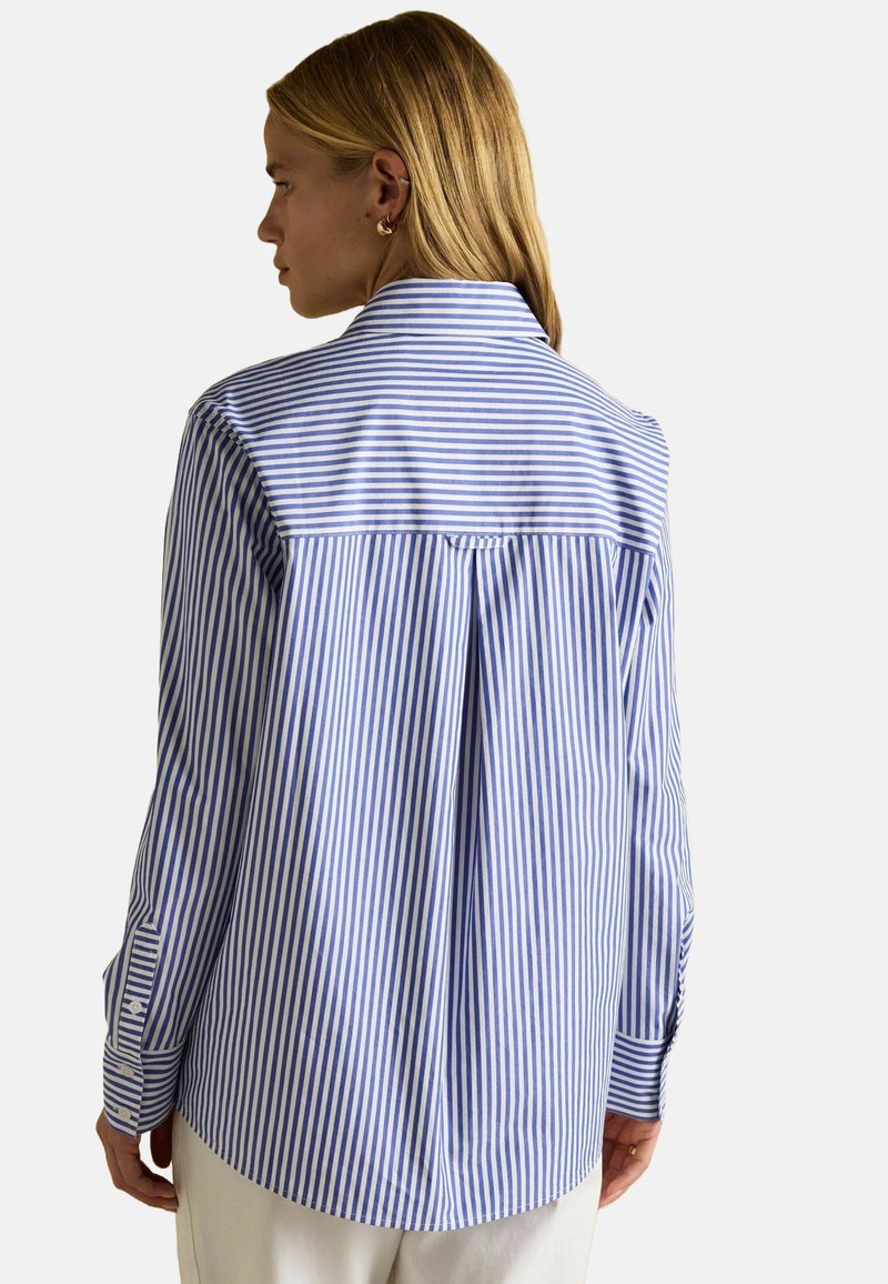 Modrá a biela pruhovaná košeľa s plisovaním na chrbte, zapínaním na gombíky na manžetách a klasickým golierom. Vyrobená z ľahkého materiálu.