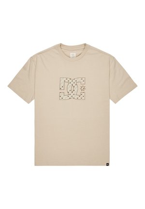 Beżowa koszulka z krótkim rękawem z centralnym, pikowanym logo DC oraz detalem w kształcie gwiazdy, okrągły dekolt i mała czarna metka przy dolnym brzegu.