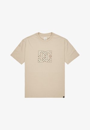 Beżowa koszulka z krótkim rękawem z centralnym, pikowanym logo DC oraz detalem w kształcie gwiazdy, okrągły dekolt i mała czarna metka przy dolnym brzegu.