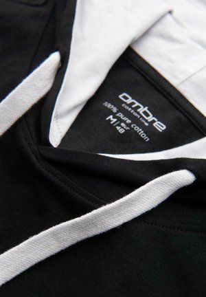 Haut à capuche noir avec des cordons blancs et une doublure intérieure, affichant une étiquette indiquant "ombre cotton lines 100% pur coton M|48".