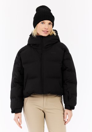 Schwarze Daunenjacke mit hohem Kragen, Reißverschluss vorne und Seitentaschen. Kombiniert mit einer schwarzen Strickmütze. Glatte Textur und taillierte Passform.