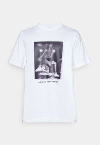 White cotton t-shirt featuring a graphic print of a basketball player and text "adidas basketball" below the image. Short sleeves and crew neckline.