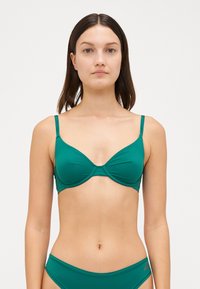 Teal bikini topp med undertråd, justerbare stropper og sømdetaljer i midten. Myk, glatt stoff med minimal merking.