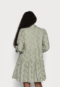 Ljusgrön klänning med ett lagerdesign, puffärmar och intrikata utskärningar i hela plagget. Texturerad tyg med en flödande form.