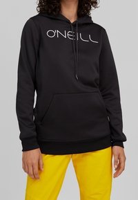 Sudadera con capucha negra con bolsillo delantero, logo en letras blancas, capucha con cordón y puños acanalados, combinada con pantalones amarillos. Material suave.