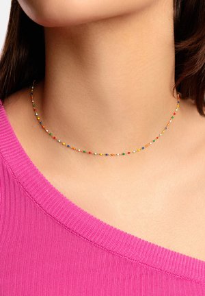 Collana choker colorata con perline piccole e rotonde di vari colori su una sottile catena dorata. Indossata sopra un top rosa a coste.