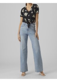 Svart blommig croptopp med korta ärmar och knytframsdetalj, kombinerad med ljusblå höga vida jeans och vita klacksandaler.