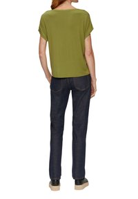 Groene korte mouw top met opgerolde mouwen, gecombineerd met een donkerdenim jeans met contrasterende stiksels en een taps toelopende snit, gedragen met zwarte schoenen.