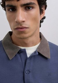 Long-sleeve polo with a dark blue body and a brown corduroy collar, featuring two buttons and a small logo on the chest.