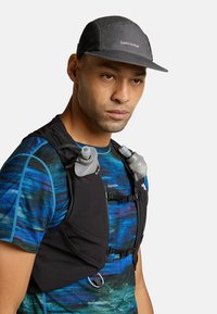 Gilet idratante nero con due borracce grigie, indossato sopra una maglietta atletica blu e testurizzata. Cappellino grigio con il logo "icebreaker" frontale.