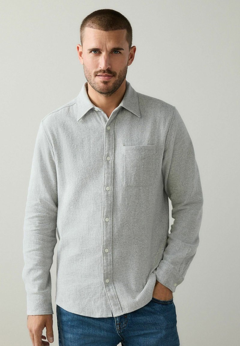 Pilkas flanelinis marškinis su mygtukų užsegimu, viena krūtinės kišenė ir ilgos rankovės. Minkšta tekstūra ir šiek tiek laisvas siluetas.