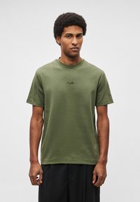 Īss piedurkņu krekliņš olīvu zaļā krāsā, izgatavots no kokvilnas, ar apaļu kakla izgriezumu un smalku izšuvumu uz krūtīm. Gluda, mīksta tekstūra.