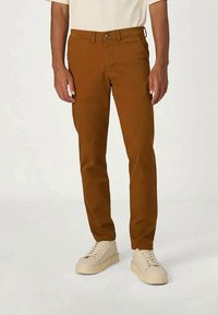 Braune Chinos aus Baumwolle mit schmalem Schnitt, Seitentaschen und Knopfverschluss. Kombiniert mit offwhite Sneakern.