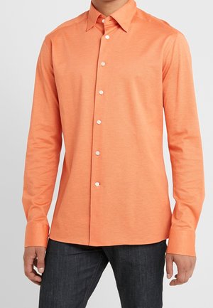 Camisa de botones de manga larga de color naranja con cuello, que presenta botones blancos y una textura suave, combinada con jeans de mezclilla oscura.