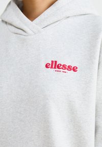 Primo piano di una felpa grigia chiara con logo rosso "ellesse" e il testo "Dal 1959" sul lato sinistro del petto.