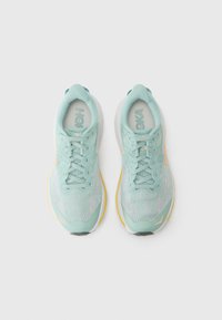 Helle blaue Sportschuhe mit einem strukturierten Strickoberteil, runder Zehenpartie und heller gelber Sohle. Mit Schnürsenkeln und einem gestickten Logo auf der Zunge.