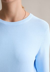 Lichtblauwe, gebreide trui met een geribbelde ronde hals en een gestructureerde textuur; beschikt over naadloze schouders en aansluitende mouwen.