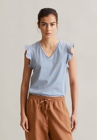 Gestreiftes blau-weißes Kurzarmoberteil mit V-Ausschnitt und Rüschendetails, kombiniert mit braunen Jogginghosen mit Kordelzug. Glattes Baumwollmaterial.