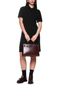 Schwarzes strukturiertes Kleid mit kurzen Ärmeln, kombiniert mit einer burgunderroten Lederhandtasche mit metallic Verschluss und passenden Schuhen mit schwarzen Socken.
