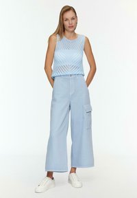 Jasnoniebieski bezrękawnik wykonany z dzianiny z wzorem w zygzak, zestawiony z jasnoniebieskimi spodniami cargo o szerokim kroju, z bocznymi kieszeniami i luźnym fasonem.