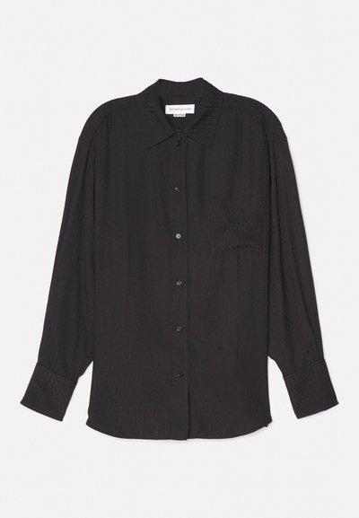 Must beest pikkade varrukatega must shirt, mis on valmistatud kergest kangast, nupuga esiosa, ühe rinnatasku ja lõdva lõikega, millel on õrn tekstuur.