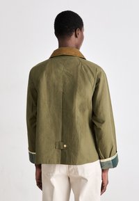 Casaco verde-azeitona com colarinho de veludo corduroy, apresentando um corte descontraído, punhos listrados e fecho de botão na parte de trás.