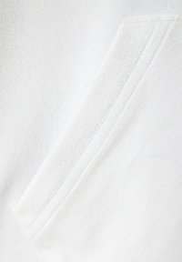 Gros plan d’un tissu blanc montrant une couture diagonale avec un double surjet sur un matériau doux et texturé.