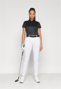 Μαύρο πόλο με κοντά μανίκια, λευκό, εφαρμοστό παντελόνι, μαύρη ζώνη και λευκά αθλητικά παπούτσια. Κρατάει ένα γκολφ μπαστούνι, φοράει γάντι στο αριστερό χέρι.