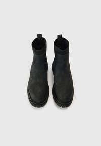 Ghete negre până la gleznă, cu finisaj mat și neted, părți laterale elastice și talpă groasă, texturată din cauciuc. Design minimalist, fără elemente vizibile de prindere.