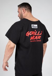 Zwarte T-shirt met korte mouwen met verhoogde textuur, "GORILLA WEAR" logo in het rood op de achterkant, en een klein label aan de hals.